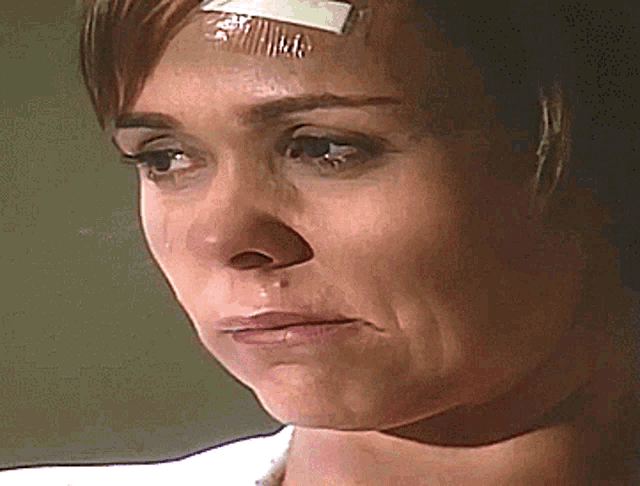 a woman with a bandage on her forehead has a tear coming out of her eye