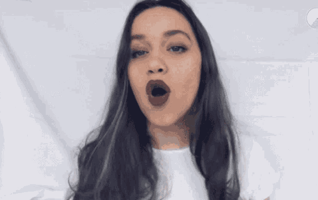 a woman with long dark hair is wearing a white shirt and making a funny face .