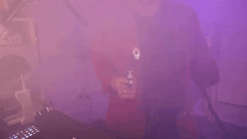 a man in a red jacket is pointing a gun at the camera in a purple room .