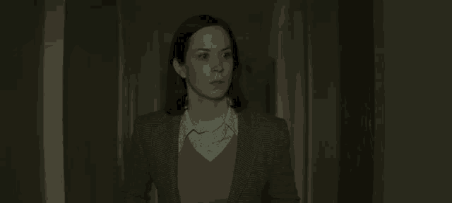 a woman in a suit and pink sweater is standing in a dark hallway .