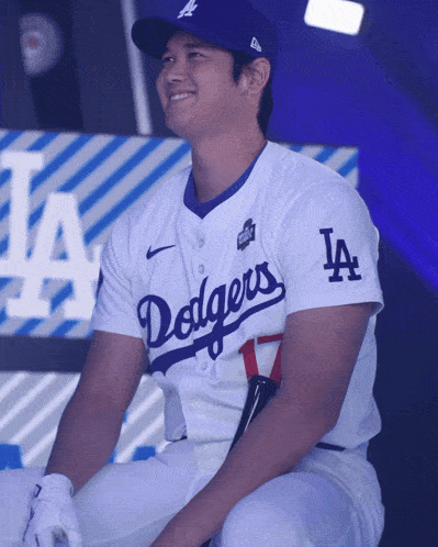a man wearing a dodgers jersey sits on a bench