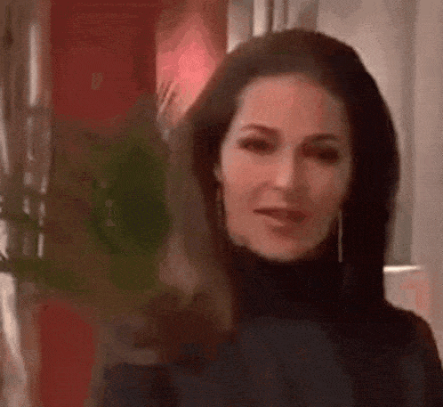 a woman with long dark hair is wearing a black turtleneck and earrings and looking at the camera .