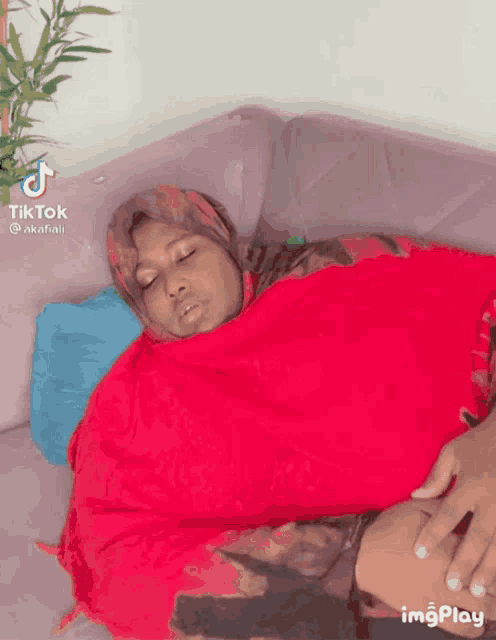 a woman wrapped in a red blanket is sleeping on a couch with tiktok written on the bottom