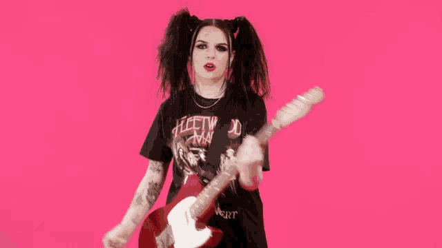 a woman wearing a fleetwood mac shirt is playing a guitar