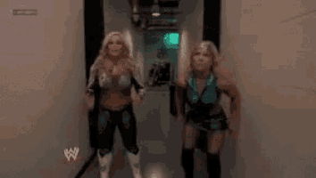 two women are walking down a hallway with a w logo on the wall behind them