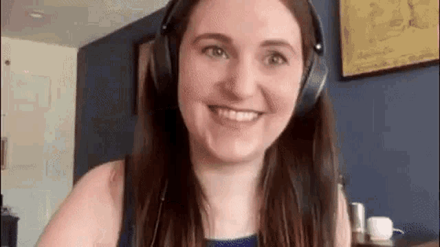 a woman wearing headphones is smiling and looking at the camera while sitting at a table .