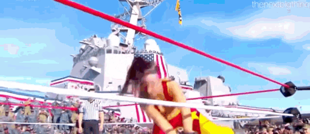 a woman is wrestling in a ring in front of a large military ship .