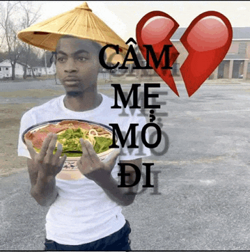 a man wearing a conical hat is holding a bowl of food with a broken heart behind him that says cam me mo di