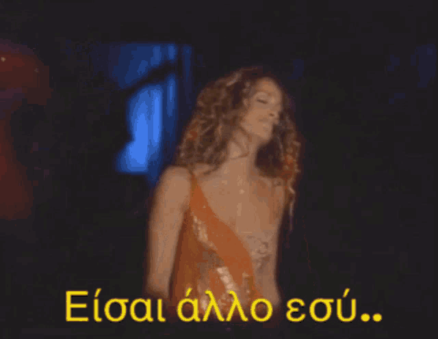 a woman in an orange dress is dancing in front of a sign that says eisai aalo sou