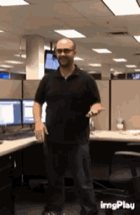 a man in a black shirt is standing in a cubicle in front of a computer monitor