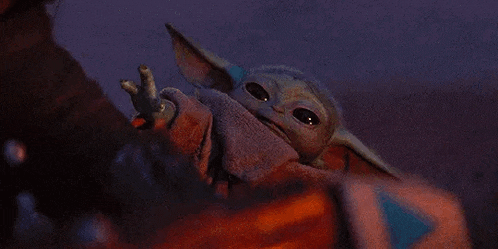 a baby yoda from star wars is waving at the camera while sitting on a person 's lap .