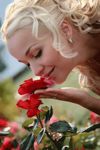 a blonde woman smelling a red rose with her hand