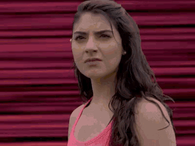 a woman in a pink tank top is standing in front of a pink wall