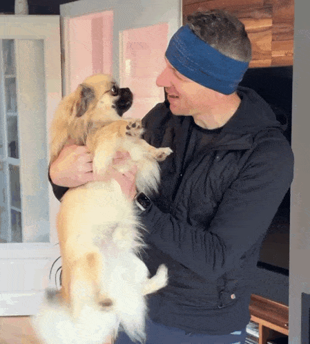 a man wearing a blue headband holds a small dog in his arms