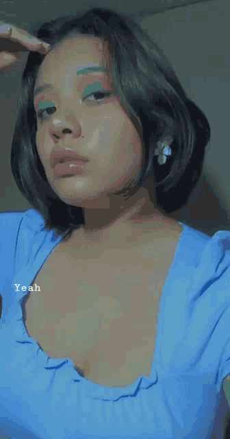 a woman wearing a blue top with a flower earring is taking a picture of herself .