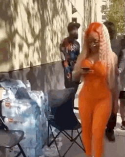a woman in an orange jumpsuit is walking down the street and looking at her phone .