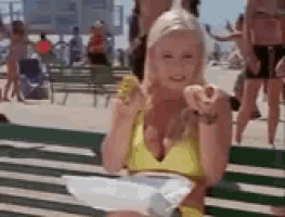 a woman in a yellow bikini is sitting on a bench eating a donut