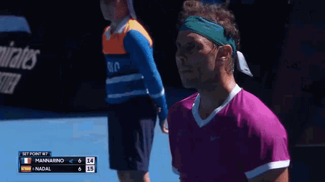 a tennis player wearing a headband and a pink shirt is looking down at the scoreboard .