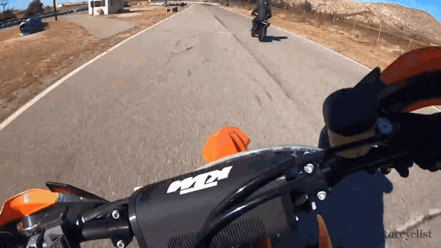 a person riding a motorcycle on a road with a ktm logo on the handlebars