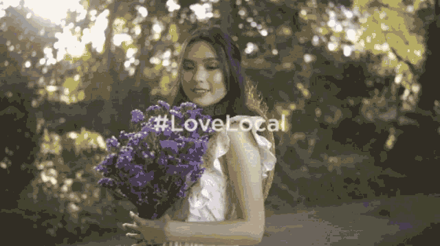a woman in a white dress is holding a bouquet of purple flowers with #lovelocal written on the bottom