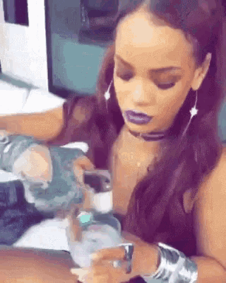 a woman with purple lipstick is sitting at a table with a glass of water .