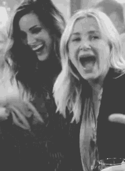 a black and white photo of two women laughing together at a table .