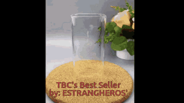a glass sitting on a cork coaster that says ' tbc 's best seller by : strangeros '