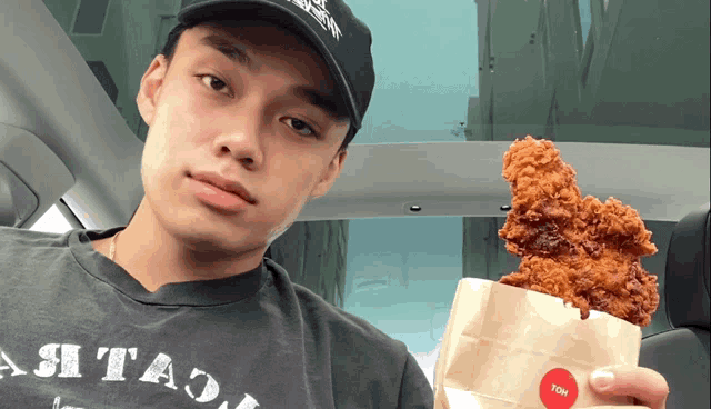 a man holding a bag of fried chicken wearing a t-shirt that says ash tao