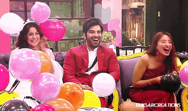 three people are sitting on a couch surrounded by balloons and laughing