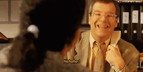 a man in a suit and tie is laughing while talking on a phone with a woman behind him .