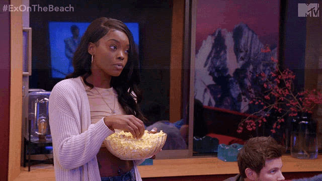 a woman is holding a bowl of popcorn in front of a tv screen that says exon the beach