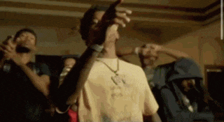 a group of young men are standing in a room . one of the men is pointing at the camera .
