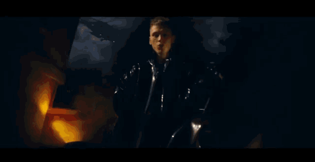 a man in a black jacket is standing in front of a flame .