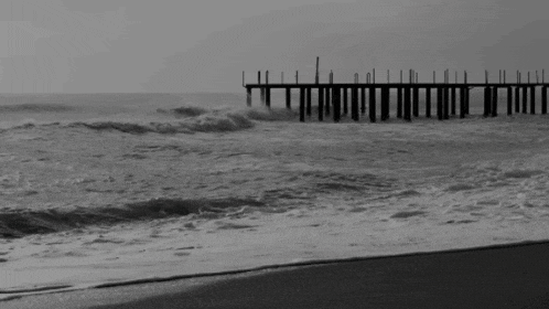 a black and white photo of a pier with waves crashing against it