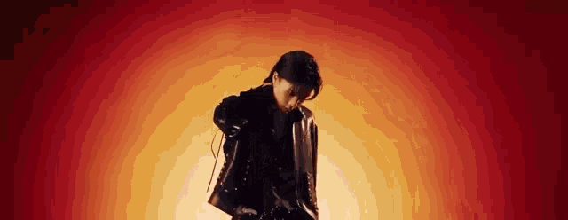 a man in a leather jacket is standing in front of a red and orange background .