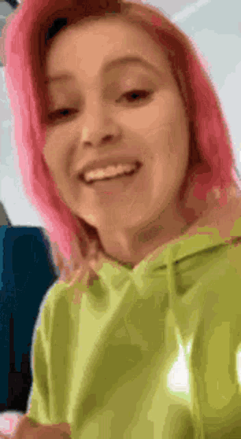 a woman with pink hair wearing a green hoodie is smiling .