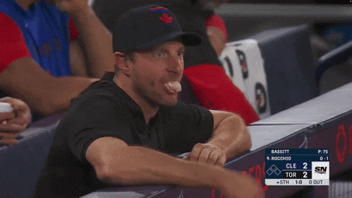 a man in a baseball cap sits in the dugout watching a baseball game