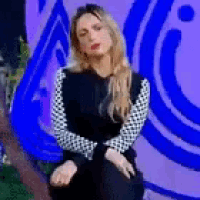 a woman in a black dress is sitting in front of a purple wall .