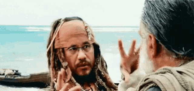 a man dressed as captain jack sparrow is talking to another man on a beach .