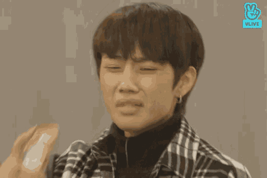 a young man wearing a plaid shirt and a black turtleneck is crying .
