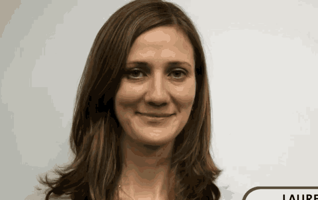 a woman with long brown hair is smiling in front of a white wall