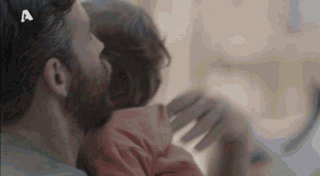 a man with a beard is hugging a woman in bed with the letter a on his head