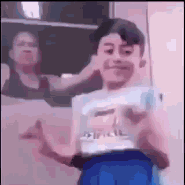 a young boy in a white shirt and blue shorts is dancing in front of a woman .