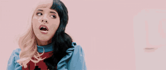 a woman with two different colored hair and a nose ring is standing in front of a pink wall with her mouth open .