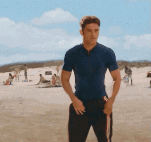a man in a blue shirt stands on a sandy beach