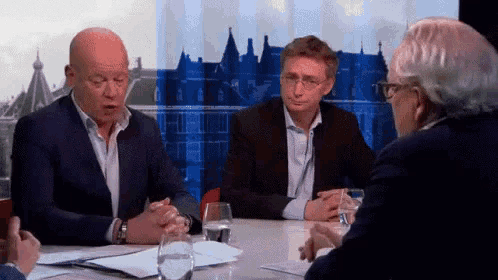 three men are sitting at a table with glasses of water and papers on it .