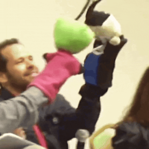 a man is holding a pink puppet and a green puppet in his hands