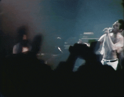 a shirtless man singing into a microphone in front of a crowd of people