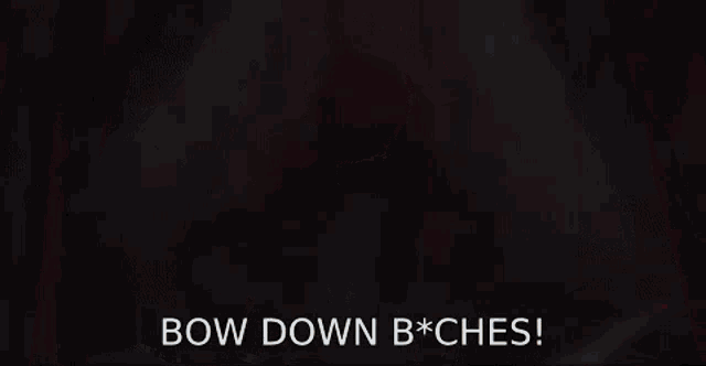 a woman in a fur coat is sitting on a bed with the words `` bow down b * ches '' written on the screen .