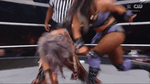 two women are fighting in a wrestling ring with a referee watching .
